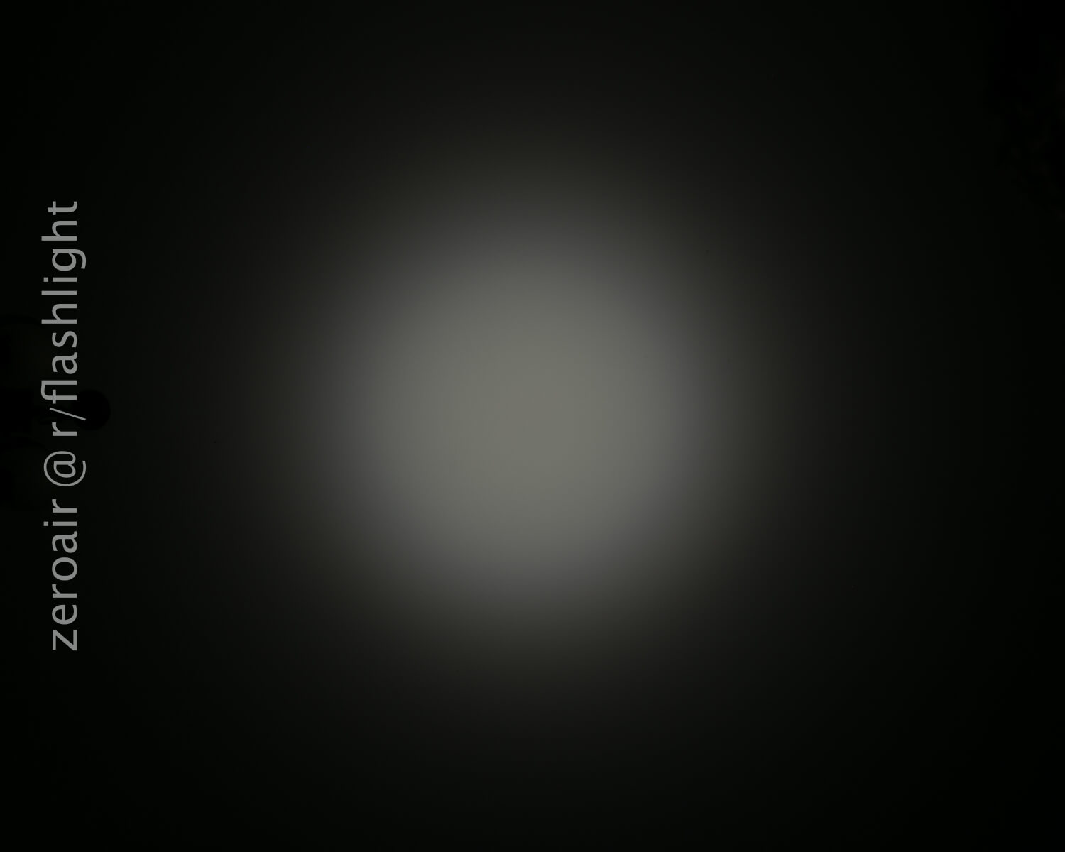 A flashlight beam creates a circular white spot with a dark, blurry outer edge against a black background. The text zeroair @ r/flashlight appears vertically on the left side.