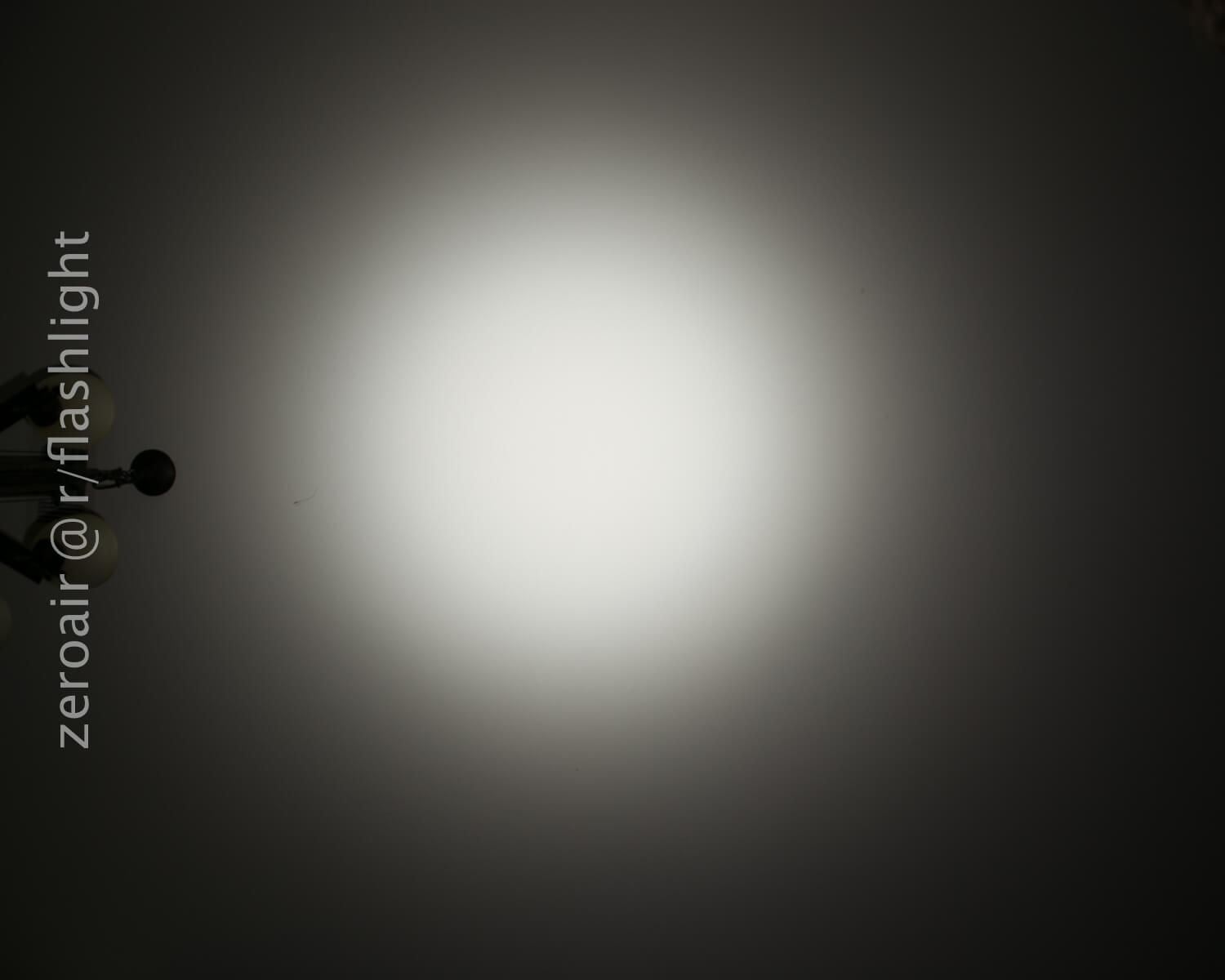 A circular white flashlight beam is projected onto a plain dark surface. The words “zeroair @ r/flashlight” appear vertically along the left side of the image.