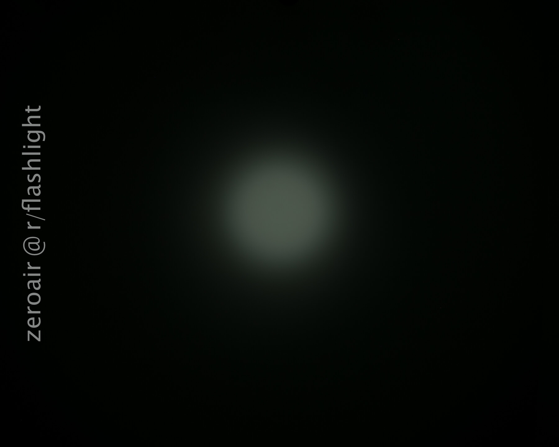 A dim, circular beam of light is visible in the center of a dark background. The text zeroair @ r/flashlight is written vertically along the left side of the image.
