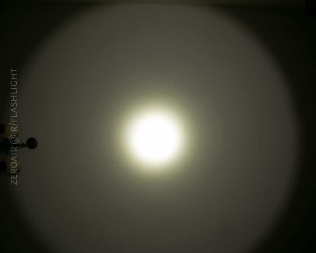 A bright circular light beam from the Eagle Eye X7 Flashlight is projected onto a blank wall in a dark room, creating a distinct central hotspot and a wider dimmer outer ring. Text reading ZEROAIR @ R/FLASHLIGHT is visible on the left side.