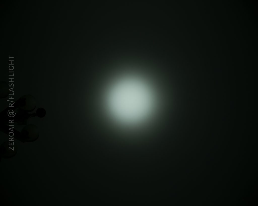 A circular white light beam shines in the center of a dark background. The left side of the image shows faint black shapes and the text ZEROAIR @ R/FLASHLIGHT written vertically.
