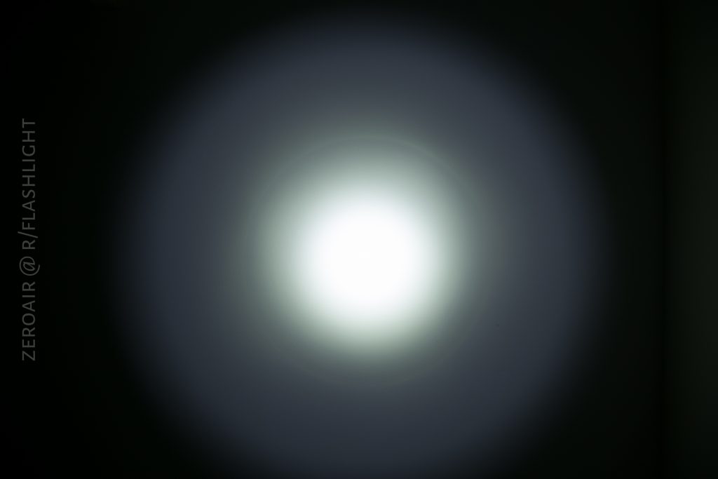 A circular beam of white light is projected onto a dark surface, creating a bright center that gradually fades outward. The text ZEROAIR @ R/FLASHLIGHT is visible along the left side.