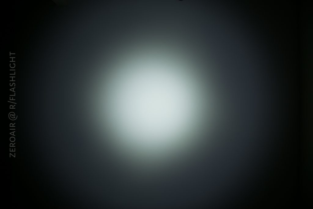 A circular white light beam shines on a dark surface, creating a bright center with a gradual fade to darkness around the edges. Text on the left reads ZEROAIR @ R/FLASHLIGHT.