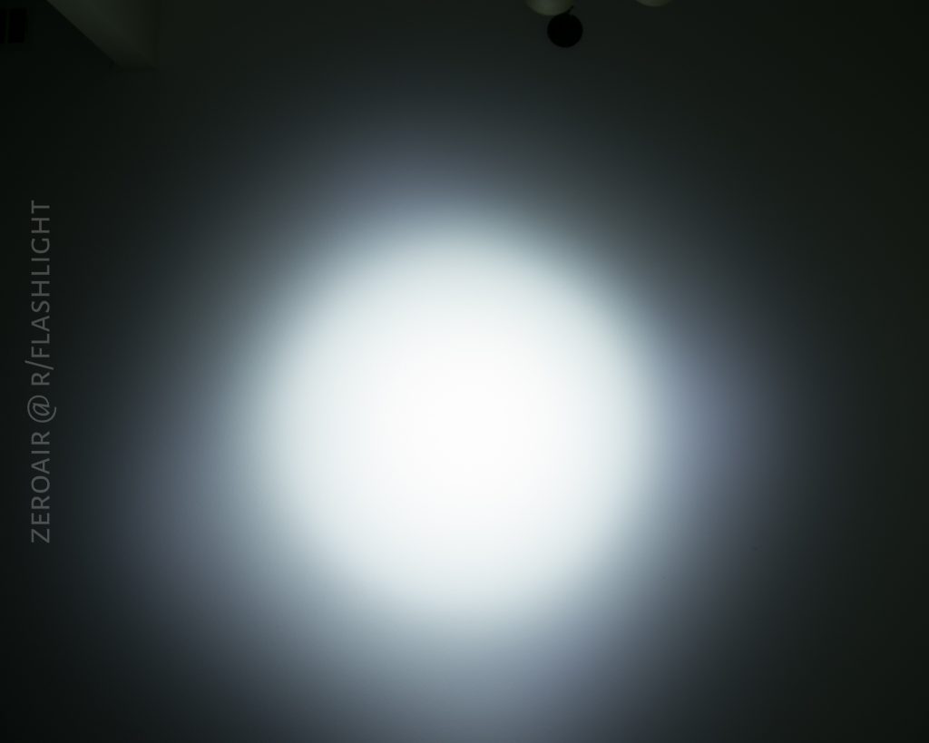 A bright white circular beam of light, likely from an Olight S1Rv2, is shown projected onto a dark surface, with the text ZEROAIR @ R/FLASHLIGHT vertically along the left side.