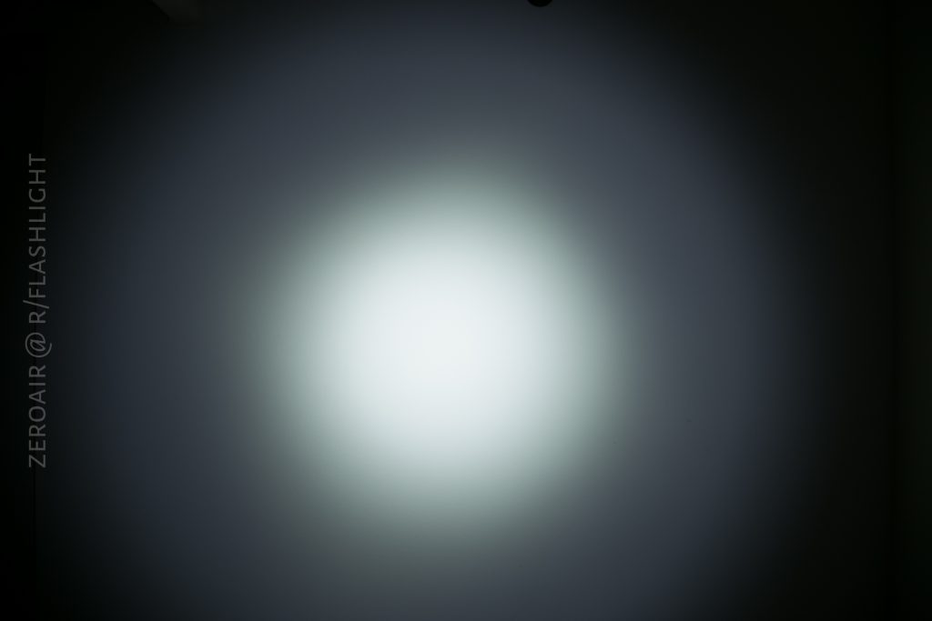 A white circular beam of light is projected onto a plain wall, creating a gradient from bright white in the center to dimmer edges. The text ZEROAIR @ R/FLASHLIGHT is vertically aligned on the left side.