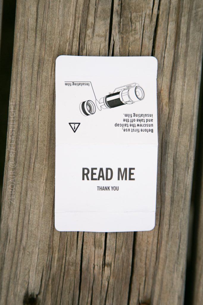 A white card on wooden boards reads READ ME THANK YOU, featuring installation instructions for the Olight S1Rv2 and a diagram of a tool printed upside down at the top of the card.