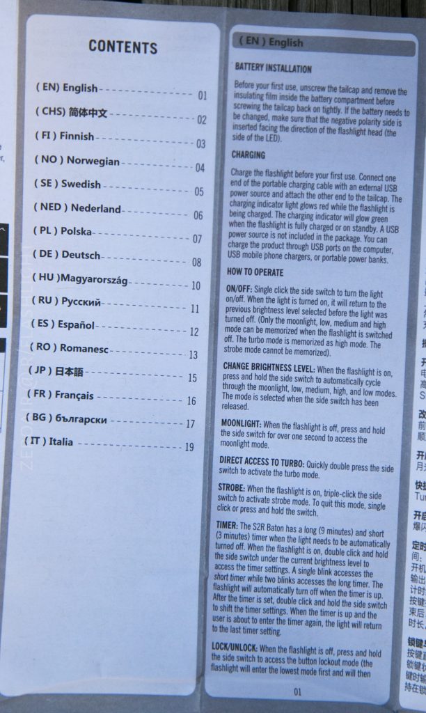 A photo of a user manual for the Olight S1Rv2. The left page lists the table of contents in multiple languages, while the right page features English instructions for battery installation, charging, operation, brightness, and timer settings.