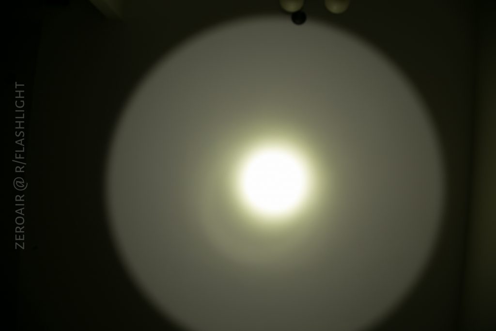 A round beam of white light is projected onto a wall in a dark room, creating a bright center and a dimmer outer ring. The text ZEROAIR @ R/FLASHLIGHT is vertically aligned on the left side.
