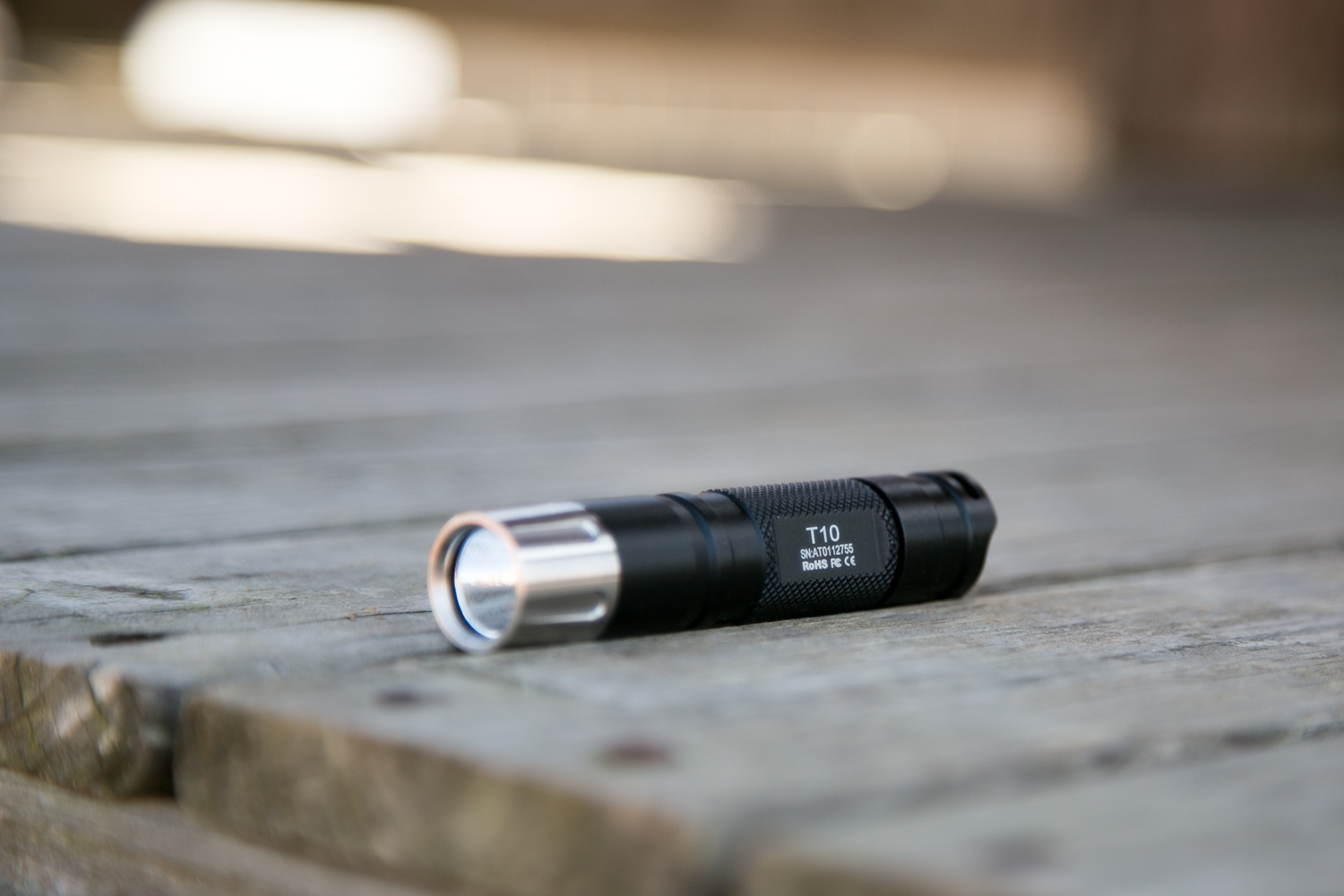 A black flashlight labeled T10 lies on its side on a weathered wooden surface, with the background out of focus.