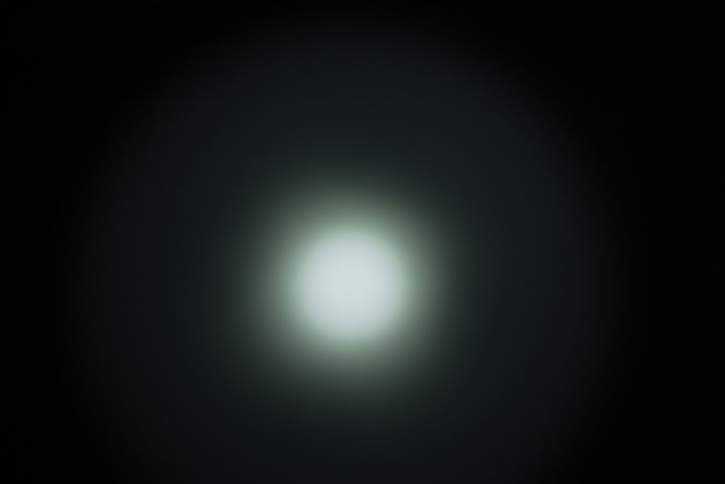 A blurred white circular light source is centered against a dark background, creating a soft glow with a gradient effect radiating outward.