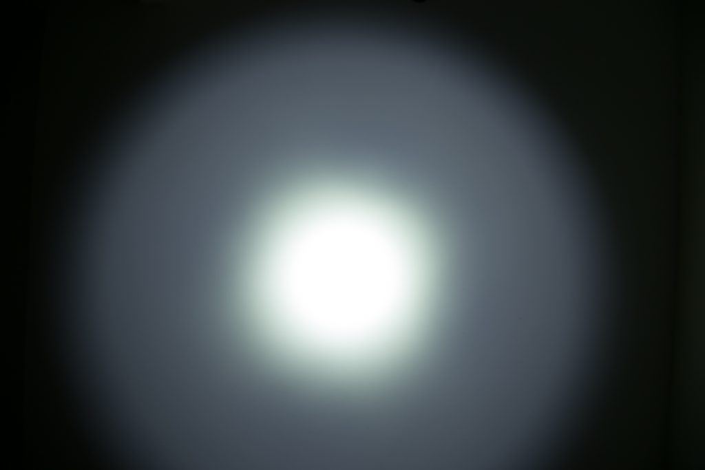 A bright white circular light is projected onto a dark surface, creating a halo effect with a strong central glow that fades outward into a dimmer gray area.