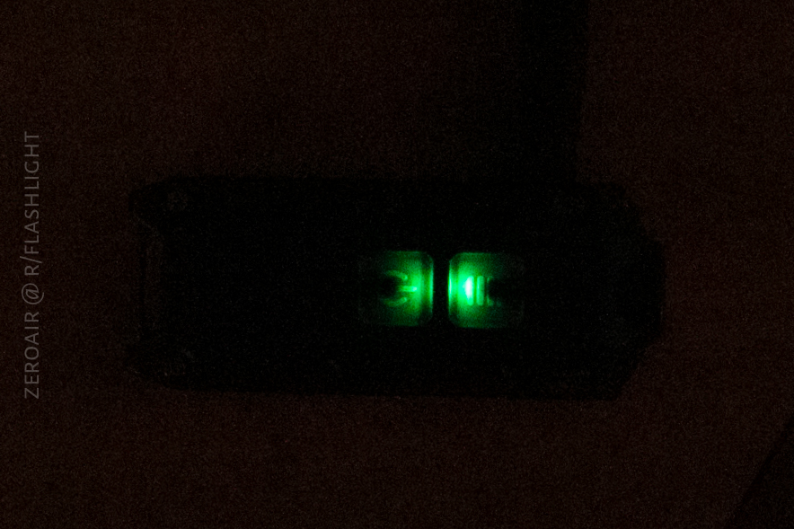 A small electronic device with two illuminated green indicator lights is visible in a dark environment. The rest of the device is mostly obscured by shadow.