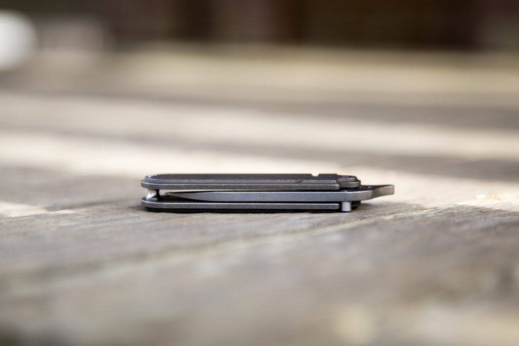 A small, closed black folding pocket knife lies flat on a wooden surface with a blurred background.