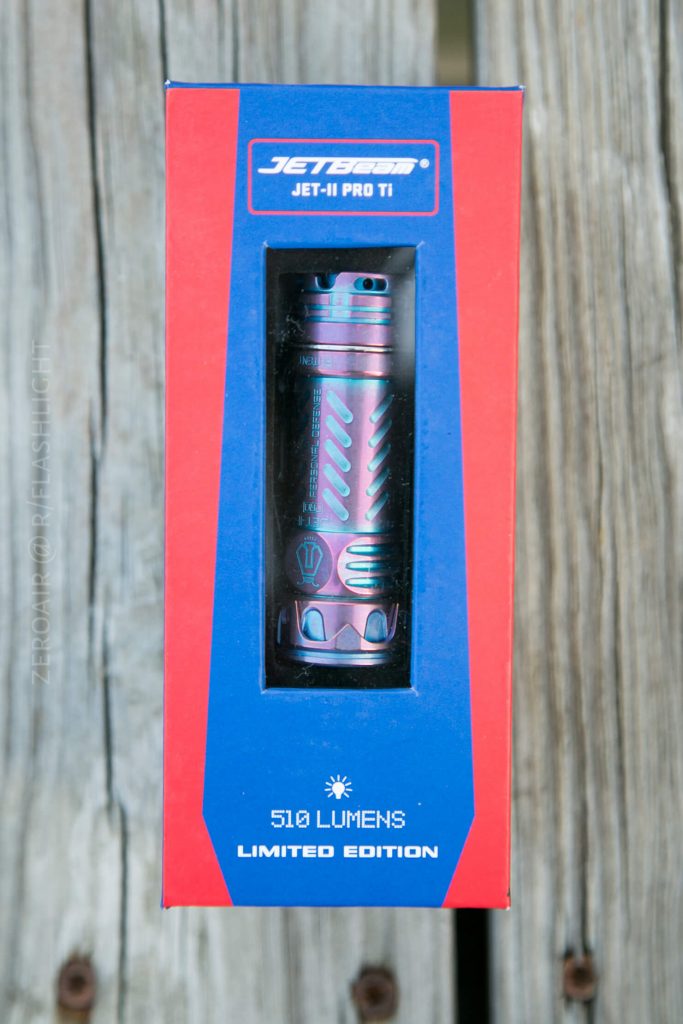 A Jetbeam Jet-II Pro Ti flashlight in a blue and red box with a clear window. The label reads 510 lumens and limited edition. The box is placed on a wooden surface.