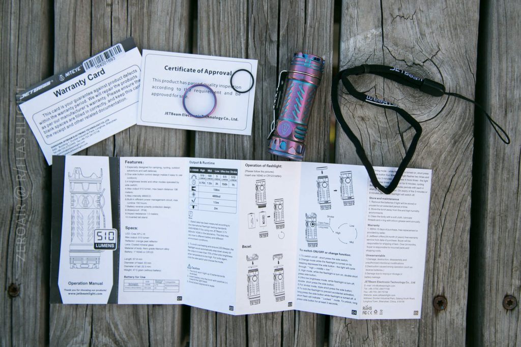 A flashlight, wrist strap, two cards, and a folded instruction manual are arranged on a wooden surface. The items are displayed clearly with diagrams and text visible on the manual.