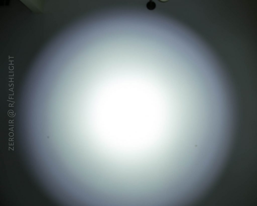 A circular beam of white light is projected onto a plain wall, creating a bright center with a gradient fading outward. The words ZEROAIR @ R/FLASHLIGHT are visible on the left side of the image.