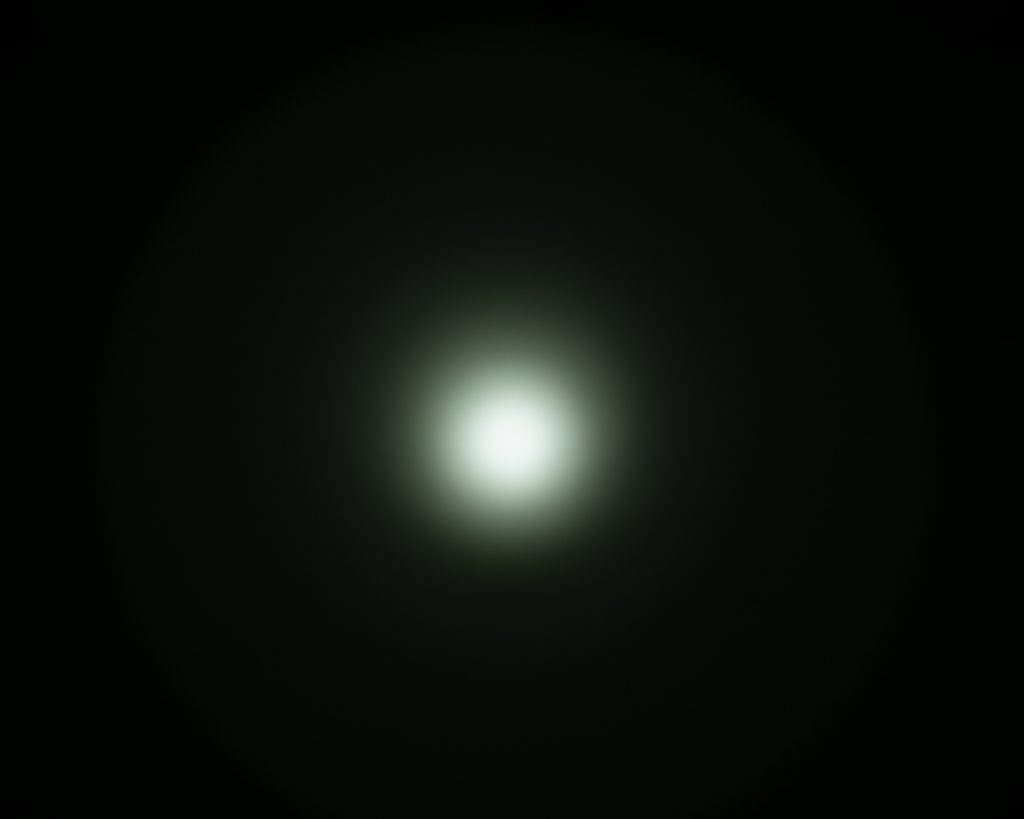A bright white circular light is centered against a dark background, surrounded by a soft halo effect that gradually fades into darkness.
