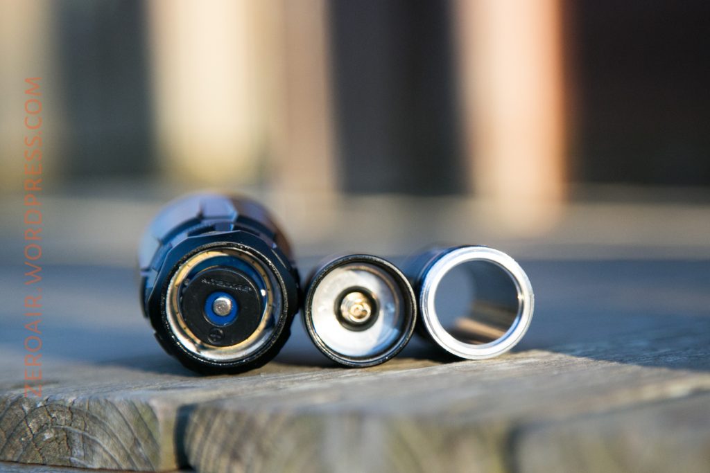 A close-up view of three cylindrical flashlight components, aligned horizontally on a wooden surface, with the words “ZEROAIR.WORDPRESS.COM” vertically along the left edge.