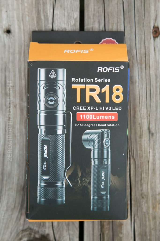 A box of the Rofis TR18 flashlight is shown. The packaging highlights features such as a CREE XP-L HI V3 LED, 1100 lumens brightness, and 0-150 degree head rotation. The box is placed on a wooden surface.