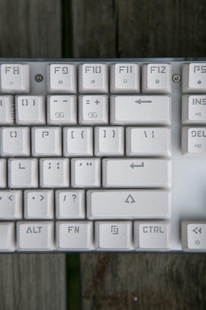 A close-up of the top right section of a white computer keyboard, showing the F8 to F12 function keys, brackets, backspace, Alt, Fn, and Ctrl keys, with a wooden surface underneath.