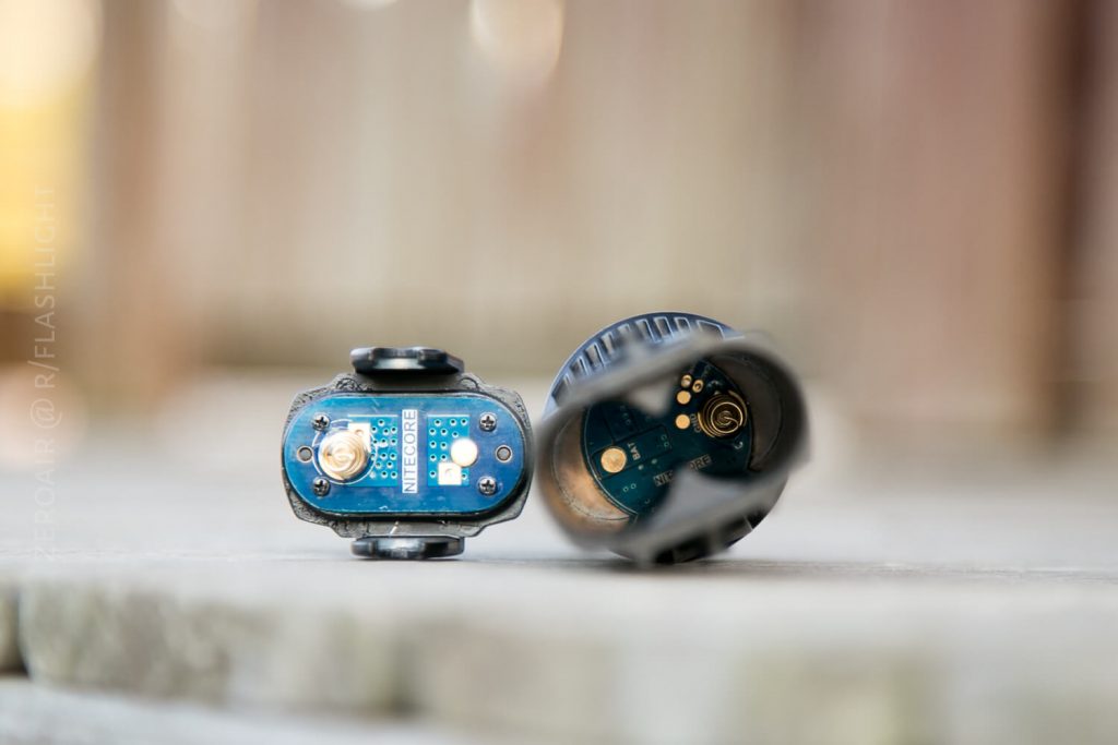 Two electronic devices are lying on their sides on a wooden surface, showing exposed circuit boards and metal contacts. The background is blurred.