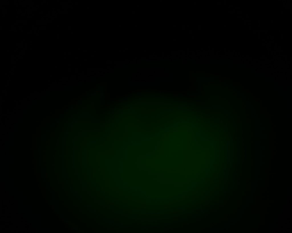 A dark image with a faint, greenish circular glow in the center, fading into the black background. No distinct shapes or objects are visible.