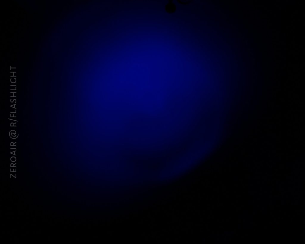 A circular blue light beam is centered against a dark background. Text on the left side reads ZEROAIR @ R/FLASHLIGHT.