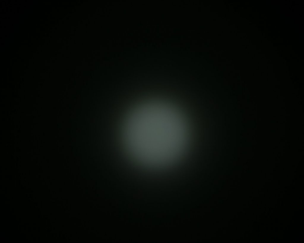 A blurry, circular white light is centered against a dark background, creating a faint halo effect. The image lacks sharp detail and distinct features.