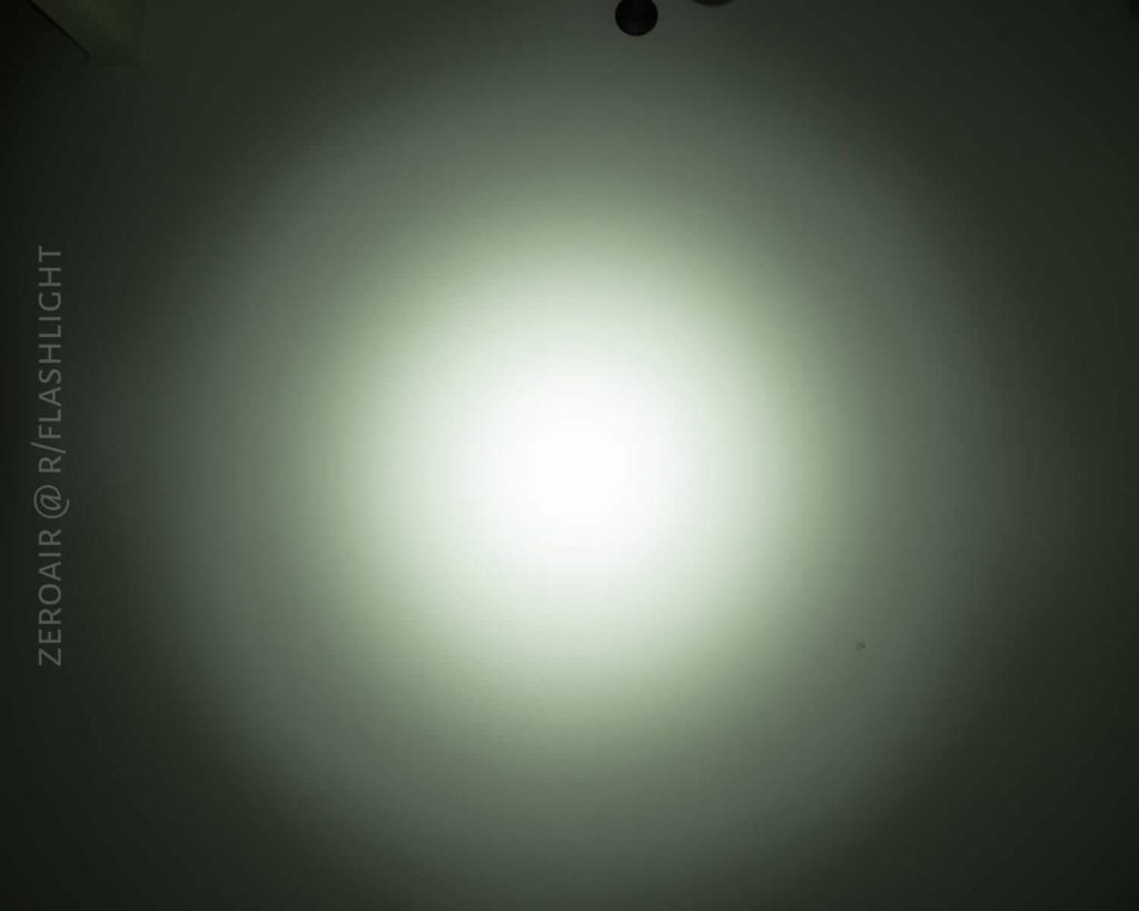 A bright, circular beam of light is projected onto a plain wall, creating a gradient from bright white in the center to dimmer light at the edges. The text ZEROAIR @ R/FLASHLIGHT is visible on the left side.