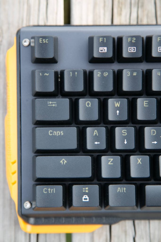Close-up of the top left corner of a black computer keyboard with yellow trim, showing the Esc, function, and letter keys on a wooden surface.