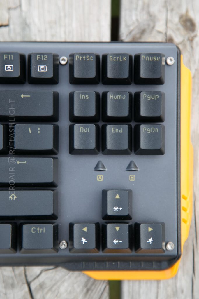Close-up of the top right section of a black computer keyboard with yellow accents, showing function, navigation, and arrow keys on a wooden surface. The keyboard features distinct, clearly labeled keys.