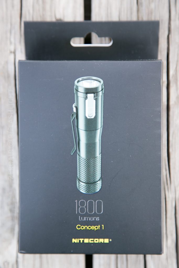 A black product box displaying an image of a Nitecore Concept 1 flashlight with 1800 Lumens, Concept 1, and the Nitecore logo printed below the image. The box is on a wooden surface.
