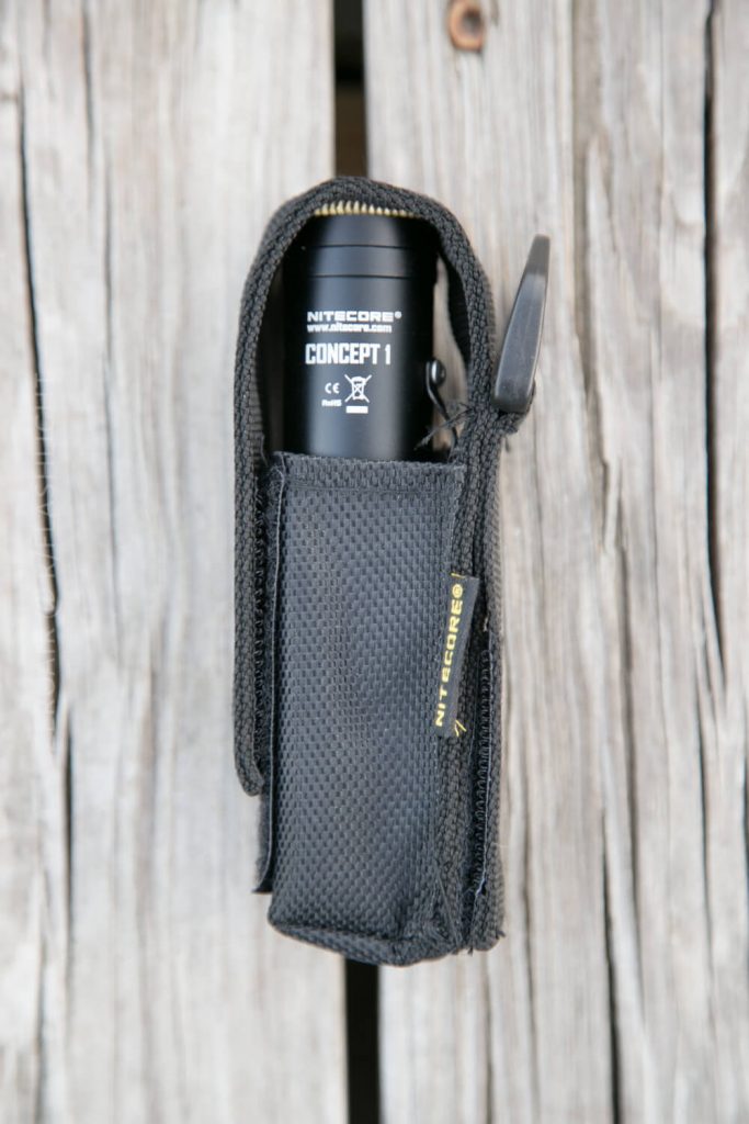 A black Nitecore Concept 1 flashlight is partially visible inside a black textured holster with a Velcro flap, placed on a weathered wooden surface.