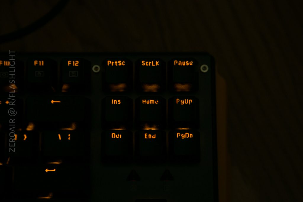 A close-up of the top-right corner of a keyboard with orange backlighting, showing the keys: PrtSc, ScrLk, Pause, Ins, Home, PgUp, Del, End, and PgDn. The background is dimly lit.