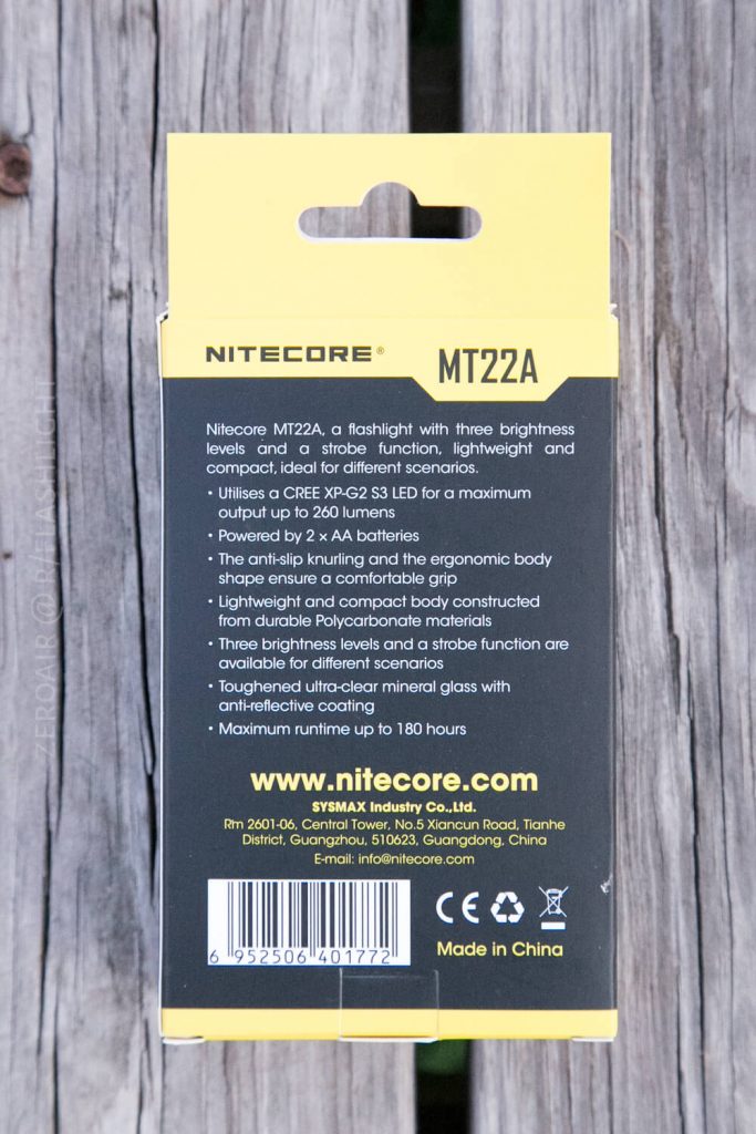 Back of a yellow and black Nitecore MT22A flashlight box on a wooden surface, showing product features, specifications, manufacturer contact details, website, and barcode at the bottom.