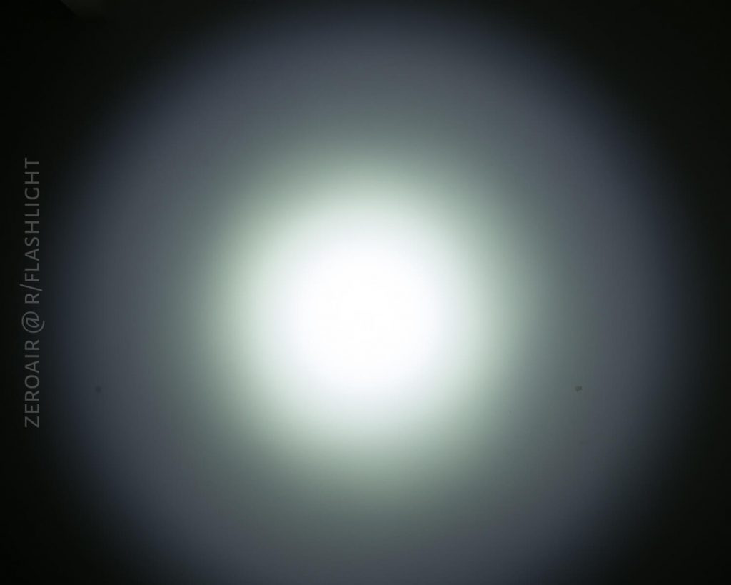A circular white light beam with a bright center gradually fades to a darker outer edge, projected onto a smooth surface. Text along the left side reads, ZEROAIR @ R/FLASHLIGHT.