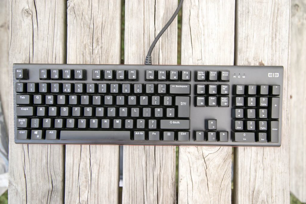 A black computer keyboard with a number pad is placed on a weathered wooden surface. The keyboard is wired and has visible function, arrow, and control keys.