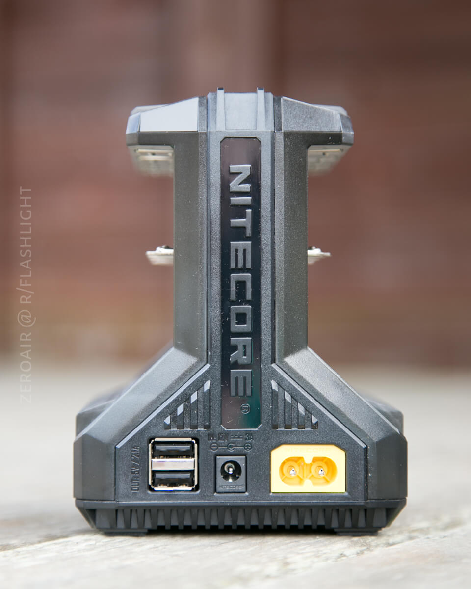 A close-up view of a Nitecore battery charger showing two USB ports, a power input, and a yellow charge connector on the front, with NITECORE branding visible on the vertical panel.