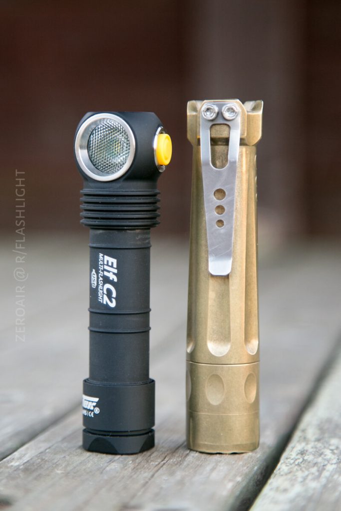 A black right-angle flashlight with a yellow button stands upright next to a brass-colored flashlight with a metal pocket clip, both placed on a wooden surface.
