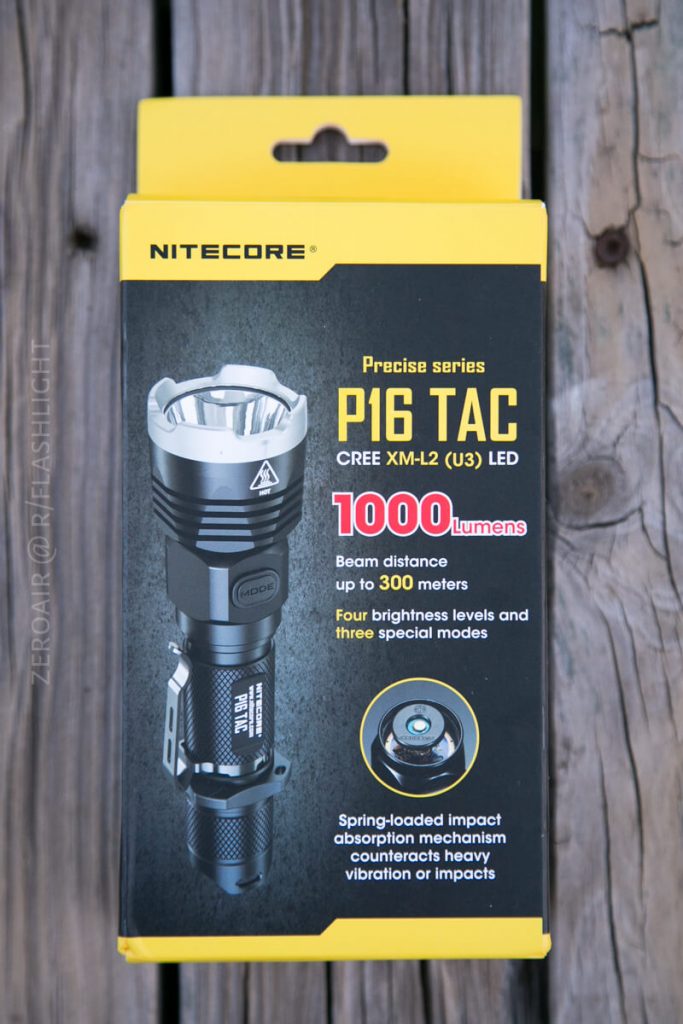 A box for the Nitecore P16 TAC flashlight is shown on a wooden surface. The packaging highlights 1000 lumens, up to 300 meters beam distance, four brightness levels, and spring-loaded impact absorption.