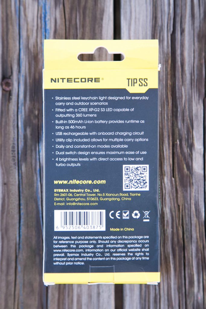 The back of a Nitecore TIP SS keychain light package showing product features, specifications, website, company information, barcode, and details about country of origin. The package is on a wooden surface.