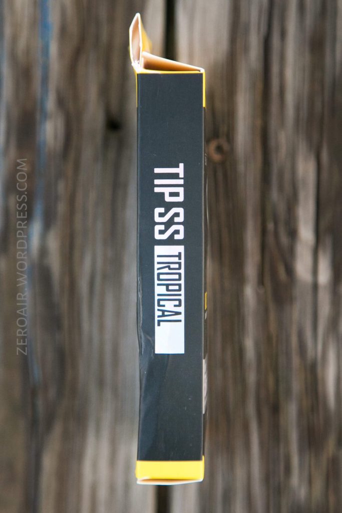 A black and yellow rectangular box labeled TIPS TROPICAL is shown from the side, placed vertically on a weathered wooden surface. The box edge displays the text ZERDAR.WORDPRESS.COM.