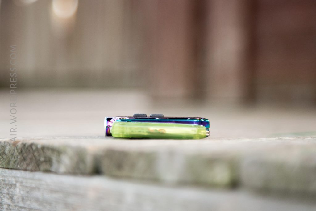 A colorful lighter lying horizontally on a wooden surface, with a blurred background and the edge of the lighter in focus.