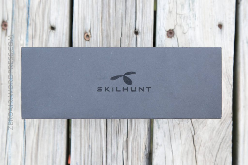 A rectangular black box with the SKILHUNT logo printed on it is placed on a weathered wooden surface. The box appears closed.