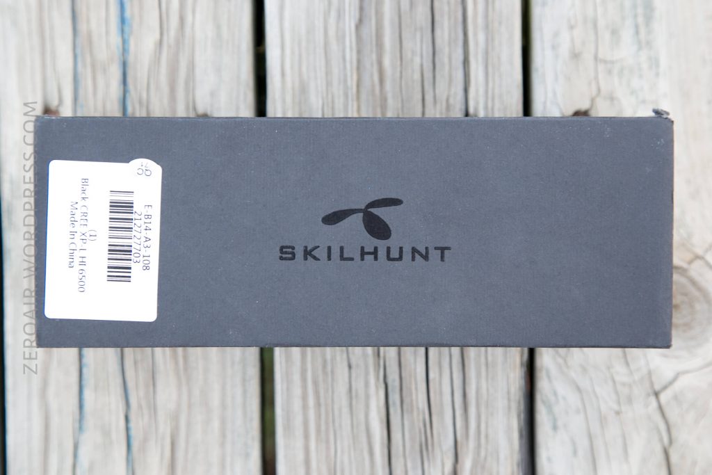 A black rectangular SKILHUNT branded box with a white product label on one side sits on a wooden surface with visible planks.