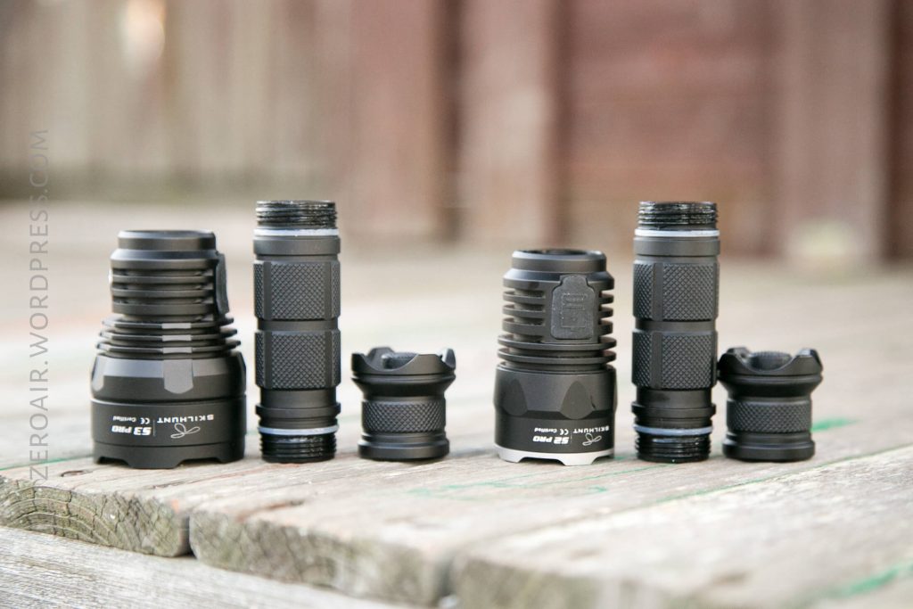 Five black flashlight bodies with textured grips stand upright on a weathered wooden surface, lined up side by side, each with different shapes and sizes, shown in natural outdoor lighting.