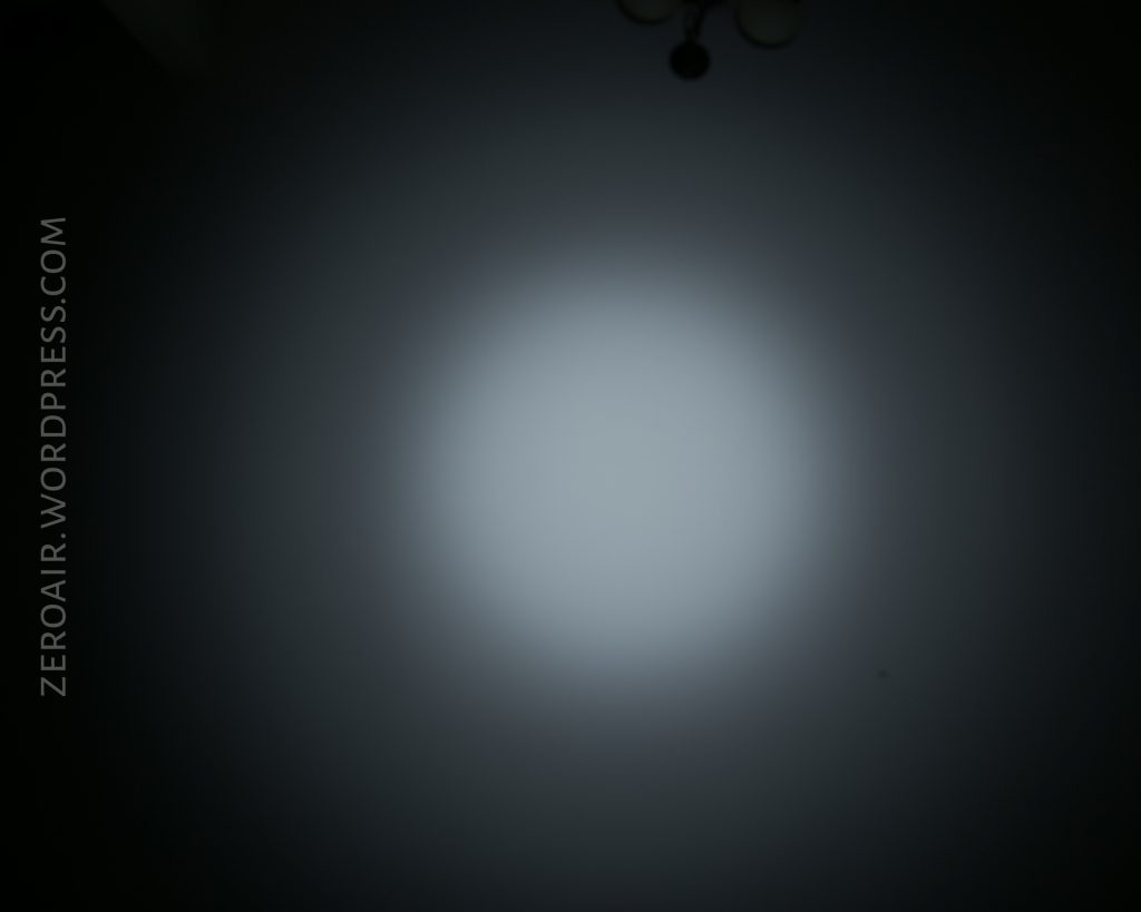 A circular beam of light is projected onto a dark wall, with the text ZEROAIR.WORDPRESS.COM written vertically along the left side. A faint ceiling light fixture is visible at the top of the image.