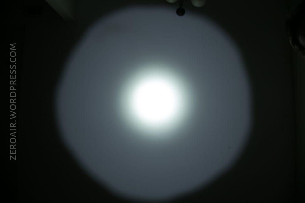 A bright flashlight beam is projected onto a dark wall, creating a circular pattern with a strong white center and a dimmer outer ring. The text ZEROAIR.WORDPRESS.COM appears vertically on the left side.