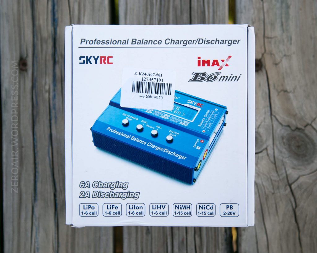 A blue SKYRC iMAX B6 mini Professional Balance Charger/Discharger is shown on a white product box with descriptions of its charging and discharging capabilities for various battery types. The box is on a wooden surface.