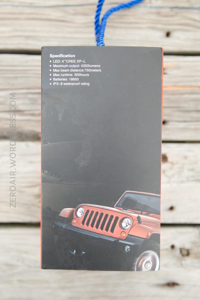 A product box shows specifications for a flashlight above an image of a red toy Jeep. Specs include LED type, max output, beam distance, runtime, and waterproof rating. The background is a wooden surface.